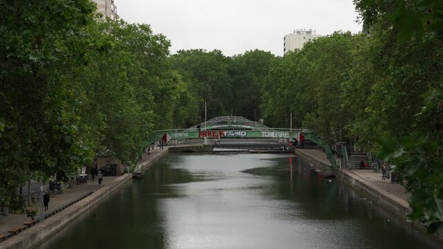 Saint-Martin canal footbridge stands in Paris France as urban water transport infrastructure where a historic pedestrian bridge and green trees waterway scenery attract tourism travel vacation.