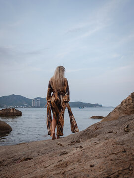 Woman in flowing abstract print beach kimono enjoying peaceful moment on rocky tropical shoreline