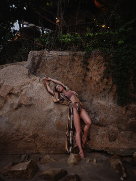 Woman in flowing abstract print beach kimono posing against natural coastal rock formation