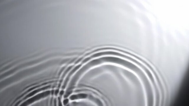 Abstract monochrome water ripples and caustic light reflections moving across a smooth white surface, featuring organic fluid wave patterns and neutral grey tones.