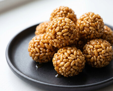 golden puffed rice balls coated in glossy caramel or jaggery syrup on white BG.