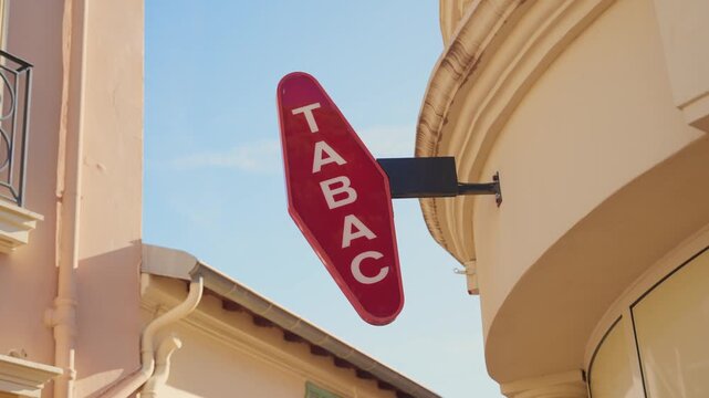 Classic red French tobacconist sign hanging on the facade of a traditional building in a European city, indicating a shop that sells tobacco products, newspapers, and lottery tickets