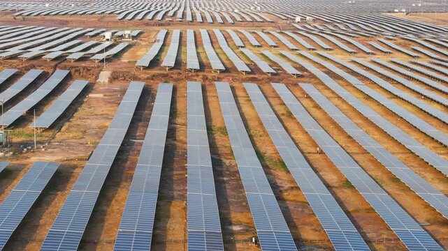 Aerial drone tilt-up revealing a vast solar farm with photovoltaic panels in geometric rows. Ideal for renewable energy, clean power, sustainability, green infrastructure, and electricity generation.