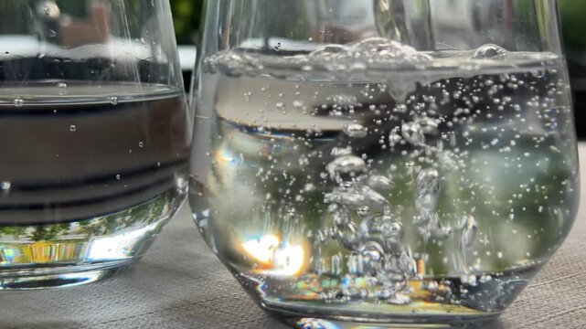 Pouring sparkling water into three drinking glasses at outdoor cafe table, refreshing beverage service before lunch, pizza and cocktails in summer restaurant