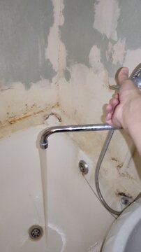Person turning water faucet in old dirty moldy bathtub with peeling plaster, vertical video