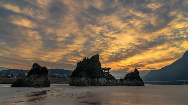 Winter sunrise timelapse of Dodamsambong Peaks with Samdojeong pavilion on rocky islands, scenic frozen river surface under a dramatic golden morning sky in Danyang, South Korea.