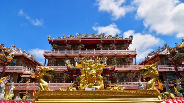 Daytime timelapse of the grand Na Jasa Tai Chue Chinese shrine in Ang Sila, featuring intricate golden dragon sculptures under a vibrant blue sky with moving white clouds, Chonburi, Thailand.
