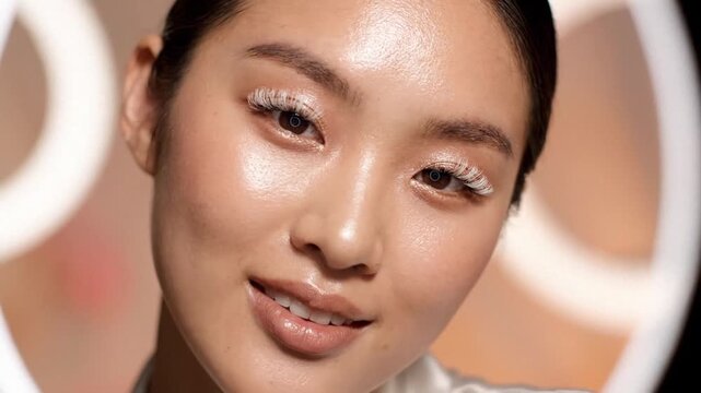 Radiant woman posing with natural makeup and glowing skin under soft studio ring lights.