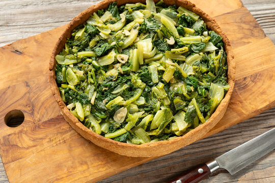 Homemade savory tart with romaine lettuce on an olive wood cutting board with a knife on the side.