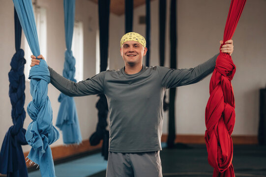 Male instructor is indoors with aerial yoga on hammock straps in a fitness studio
