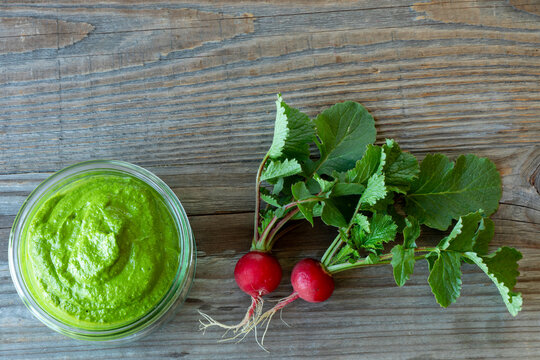 Flat lay overhead view of radish greens pesto in a glass bowl on a rustic wooden background with two whole radishes and top copy space