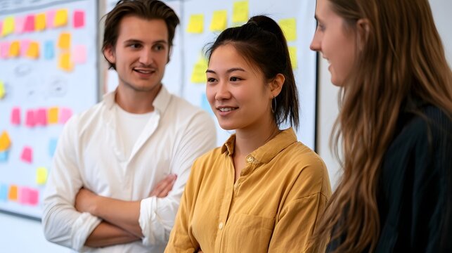 Three people collaborate around a whiteboard covered with colorful sticky notes during a team brainstorming session