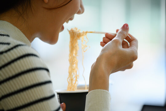 Close Up of Young Asian Woman Eating Instant Noodles from Cup with Chopsticks &ndash; Quick Convenient Meal