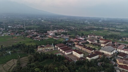 Fototapeta premium Aerial panorama of a lush valley town with schools and rice fields near mountains