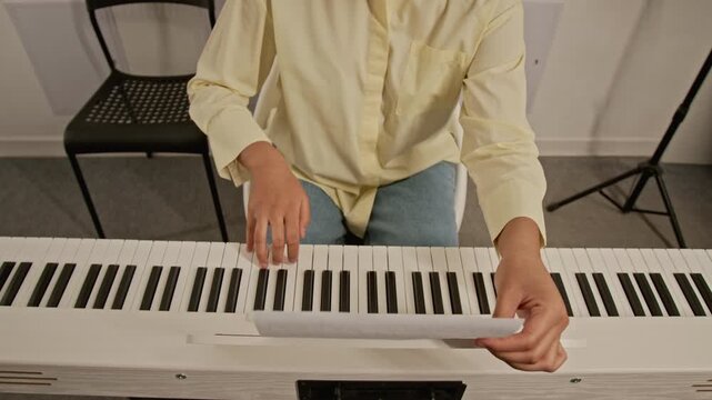 Tilt up shot of African American girl playing digital piano, adjusting sheet music on stand and practicing keys. Video for music education platforms, online tutorials, and hobby advertisements