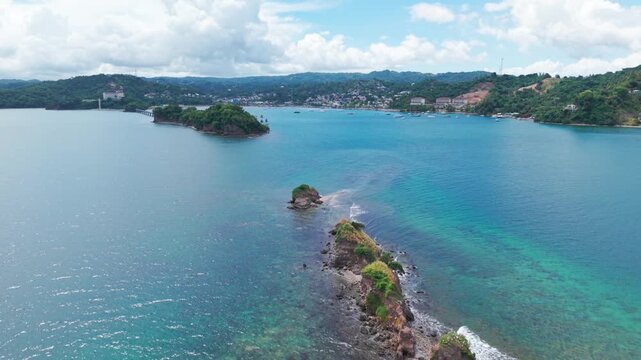 Aerial view of rugged, rocky islets rising from the turquoise waters of Saman&aacute; Bay, Dominican Republic, with lush green coastal hills in the background under a partly cloudy sky.