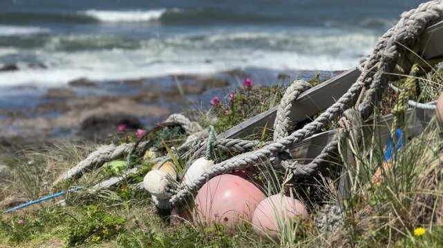 Sun-bleached foam floats hang from tangled rope lashed to a split rail fence, framed by wind-blown coastal grass.