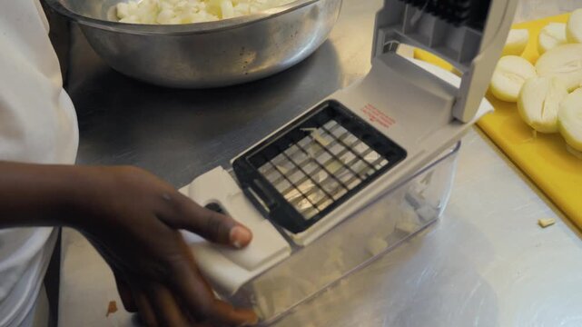 A close-up shot showing a chef in a professional kitchen emptying diced onions from a manual chopper into a bowl and then using the tool to chop another fresh onion piece