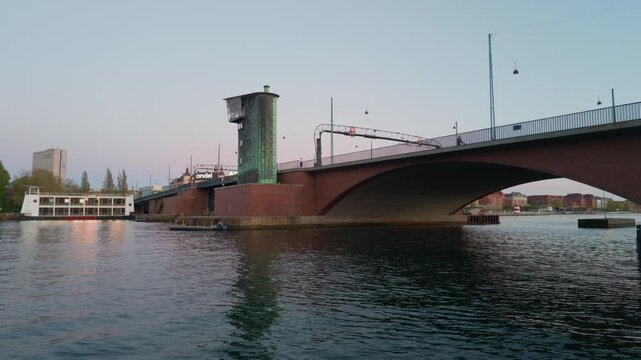Red brick bridge sunset traffic, gimbal stabilizer shot. 60fps close view walking forward along Copenhagen river approaching historic overpass with cars and bikes.