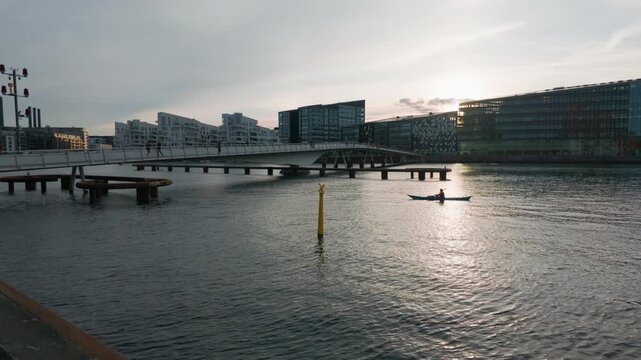 City bridge river sunset people, gimbal stabilizer shot. 60fps tracking shot walking right to left over Copenhagen stream with buildings and a person in canoe.
