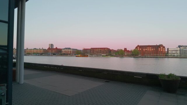 City river sunset buildings boat, gimbal stabilizer shot. 60fps cinematic push in walking forward on Copenhagen waterfront revealing a yellow ship in Denmark.