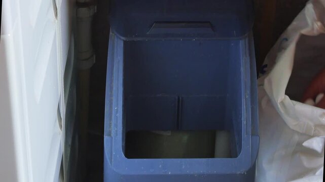 Close-up of a nan filling a water softner with salt tablets in a utility room