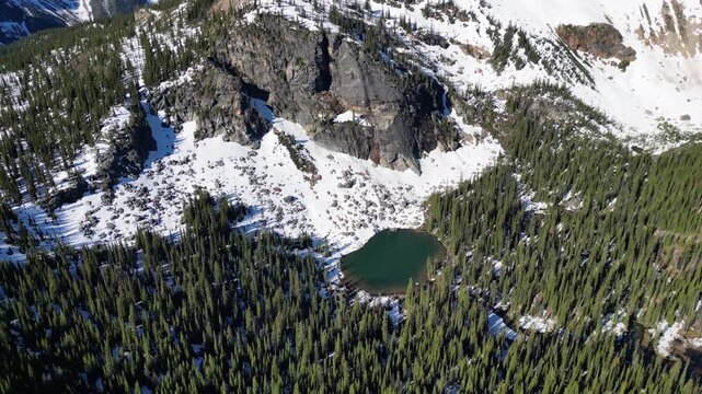 Drone shot of a mountain lake in Bristish Columbia with pine tree, melting snow in Valhalla Provincial Park.