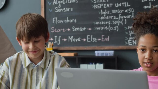 Multiethnic kids collaborating on laptop during robotics and coding lesson in classroom. Video is suitable for promoting STEM education, school enrollment, and modern learning programs