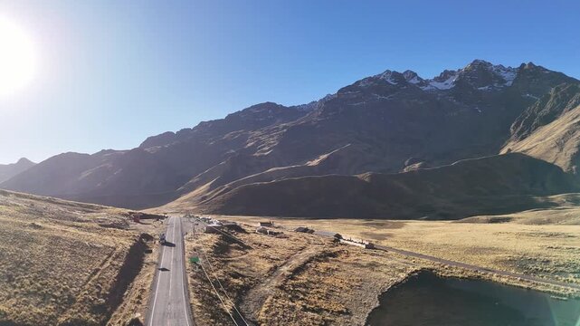 Aerial drone view of a car driving on Route 3S through La Raya Pass in Peru, with the sun shining brightly over the rugged peaks of Kunka mountain