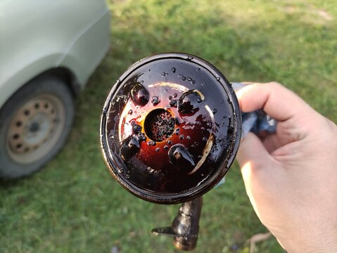 Close up of dirty engine oil strainer with sludge and bubbles held in hand