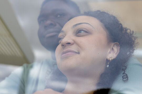 African American couple standing by large window, man wearing light sweater, earrings reflecting