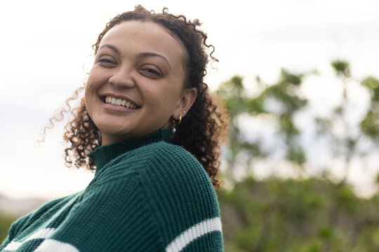 African American woman smiling, facing camera outside wearing green striped sweater and gold hoops