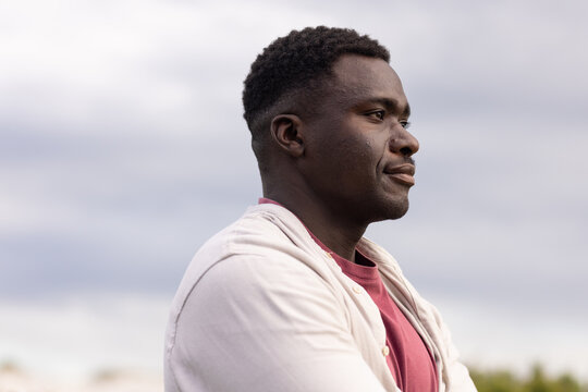 Man facing right in three-quarter profile outdoors wearing beige jacket and maroon tee, copy space