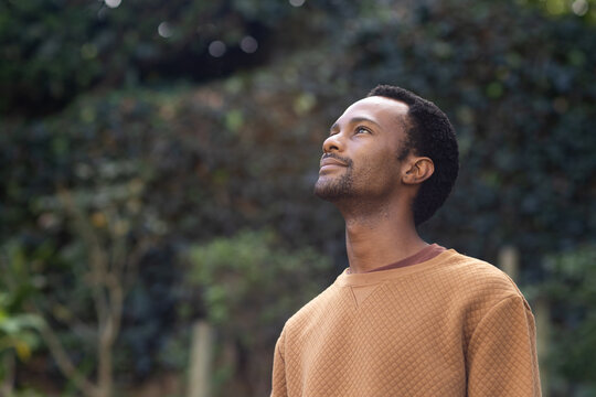 Man standing in garden wearing quilted light brown sweater with darker undershirt, copy space