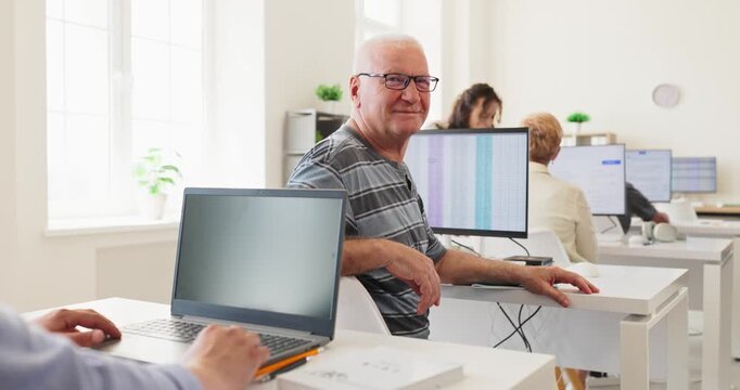 Adult student in training classroom using computer. Smiling senior participates in a course with a laptop, focusing on digital skills. Concept shows professional development and learning.