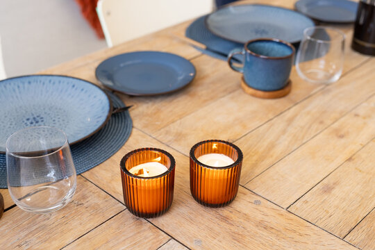 Two amber ribbed glass candles are glowing on wooden dining table with blue plates