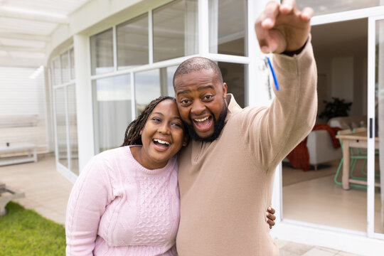 African couple standing on covered patio in front of sliding glass doors, holding blue keychain