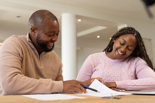 African couple reviewing docs at wooden table, woman in pink sweater, man holding blue pen, keys