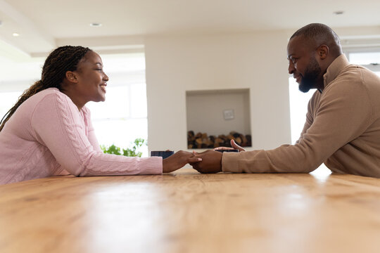 African couple wearing sweaters sitting at dining table holding hands with mug and stacked logs