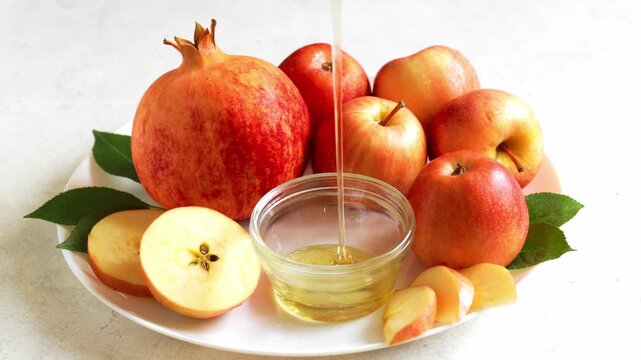Happy Rosh Hashanah. Jewish New Year holiday concept. Slow motion of honey dpipping in a bown, apples and pomegranates around.