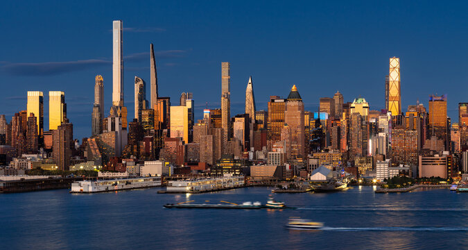 New York City panoramic evening view of Midtown Manhattan skyline from across the Hudson River, with supertall skyscrapers illuminated by the last sunset light. USA