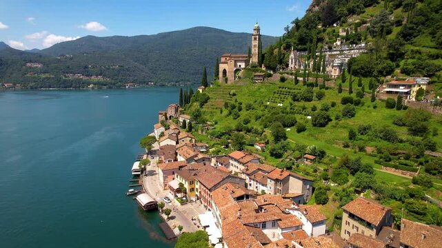Morcote Lake Lugano Switzerland 4K Drone. Side pull back aerial view of church and houses by water. Most beautiful villages Ticino canton alpine mountain valley background b roll cinematic video asset