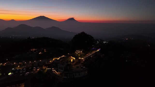 Views of the sun rising over distant peaks from a mountaintop lookout with cafes & a camping area.
silancur higland magelang