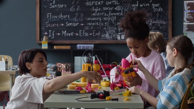 Female teacher helping multiethnic children assemble robotic toys during STEM class. Footage is perfect for promoting modern elementary education, science camps, and technology learning programs