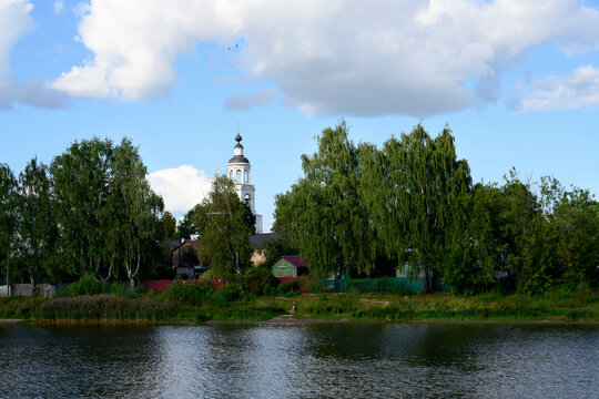 Dense trees and wooden houses on the banks of the Volga River with the bell tower of the Tolga Monastery above them, near Yaroslavl, Russia