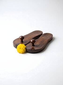 Traditional wooden Indian Khadau sandals with yellow marigold flower on white background, representing respect and devotion for Guru Purnima festival or spiritual rituals.