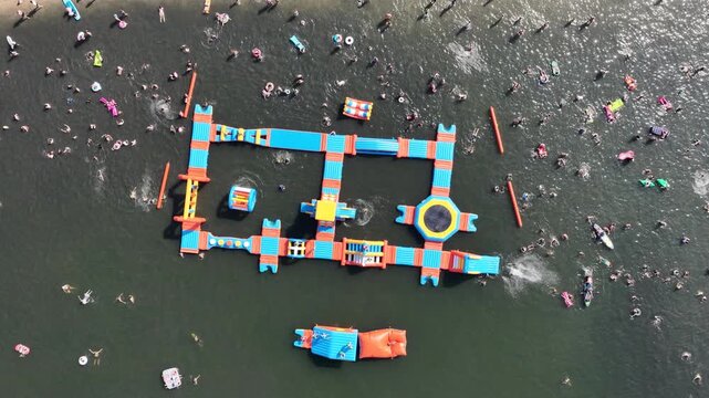 Aerial drone view of a crowded summer lake beach with people swimming and sunbathing. Colorful umbrellas, water obstacle course on lake, on a sunny day. Lake Pogoria in Dabrowa Gornicza, Poland