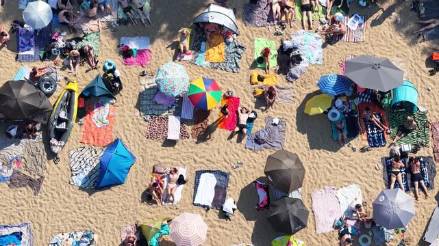 Aerial drone view of a crowded summer lake beach with people swimming and sunbathing. Colorful umbrellas, water obstacle course on lake, on a sunny day. Lake Pogoria in Dabrowa Gornicza, Poland