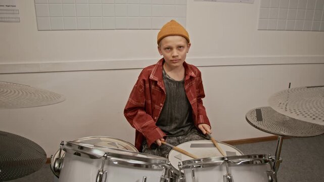 Zoom in portrait of Caucasian teenage boy sitting behind drum kit in music school, holding drumsticks and looking at camera. Footage for promoting music education and youth hobby programs