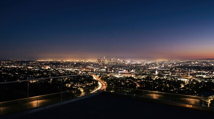 Fototapeta premium A person stands on a balcony overlooking a sprawling cityscape at night. The dark sky is illuminated by the lights of Los Angeles, stretching out towards the horizon.